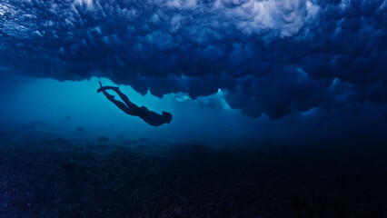 Man dives and swims underwater under the breaking wave