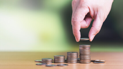 Man hand holding coin and put on the stacked coin on the table in concept of account for money saving, financial planning and retirement plan.