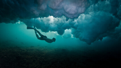 Man dives and swims underwater under the breaking wave