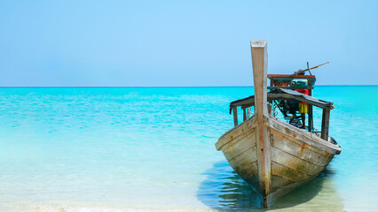 Traditional wooden long-tail boat on tropical beach with turquoise sea and blue sky. Summer vacation concept. Thailand travel scenery.
