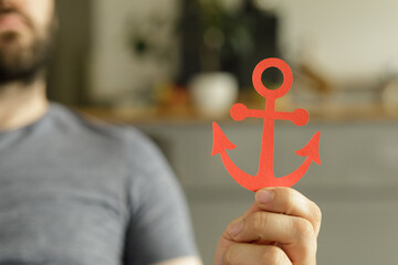 Close-up of a man holding a red paper anchor.  Concept of hope, stability, or faith. © vegefox.com