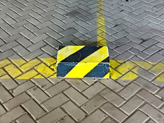 Yellow and black striped barrier block on grey herringbone pavers with a yellow line.