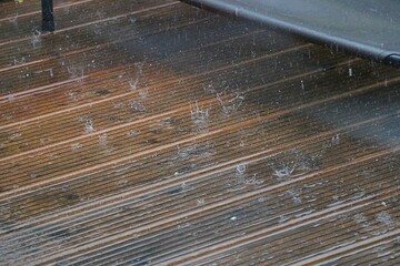 Heavy rain falls on the terrace made of wooden panels and shatters with splashing crowns