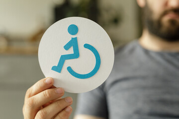 Close-up of a hand holding a paper circle with a blue accessibility symbol.
