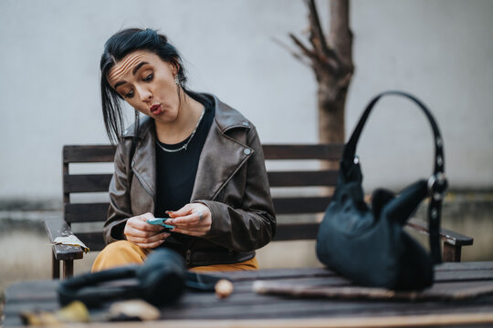 Young woman seated outdoors making an amusing surprised expression, holding an object in her hands. - Powered by Adobe