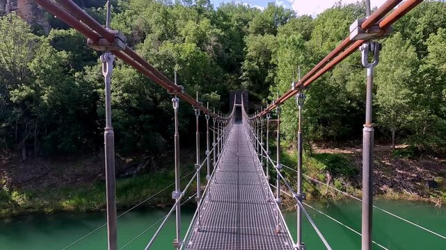A perspective view of a suspension bridge in Congost de Mont-rebei, Catalonia, showcasing the lush greenery and clear blue skies of the picturesque natural environment.