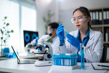 A woman in a lab coat is holding a pipette and looking at a microscope