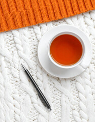 A cup of tea on a white knitted surface with a black pen beside it, bordered by an orange textured fabric