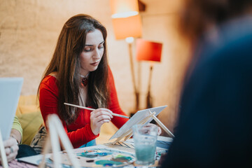 A woman engrossed in painting during a cozy indoor art workshop, surrounded by artistic tools and a vibrant ambiance, emphasizing creativity, inspiration, and relaxation in a social setting.