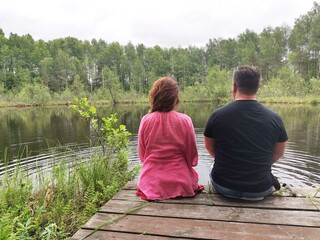 a man and a woman are sitting on the shore of a lake talking