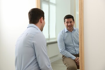 Handsome man looking at himself in mirror indoors