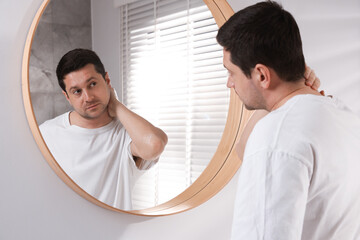 Handsome man looking at himself in mirror indoors