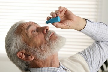 Senior man applying eye drops at home