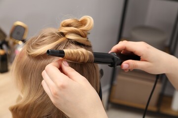 Naklejka premium Hairdresser curling woman's hair in salon, closeup