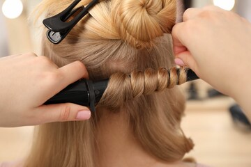 Fototapeta premium Hairdresser curling woman's hair in salon, closeup
