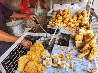 Assorted Indonesian fried snacks sold at a street food vendor stall. Popular local delicacies include tempeh, tofu, bananas, and vegetable fritters.