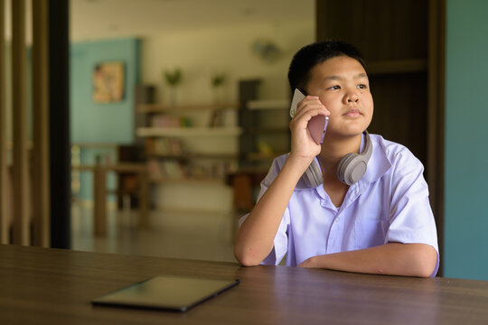 Thai Student in School Uniform Studying in Library While Talking on Phone - Powered by Adobe