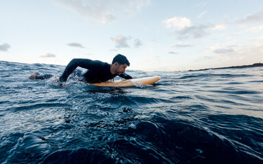 Surfer paddling on surfboard in ocean wearing wetsuit during sunset