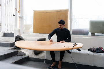 Surfer waxing surfboard in his workshop getting ready for surfing