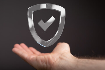 A hand holds a transparent digital shield with a checkmark, symbolizing data protection and...