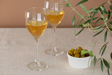 Two glasses of white non-alcoholic wine with olives and green on a table.