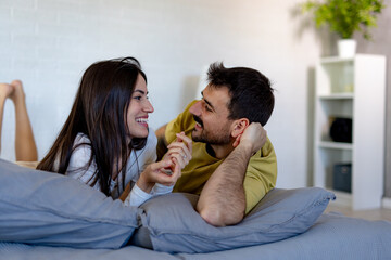 Young couple lying in bed, holding hands and chatting joyfully in the morning light, enjoying each other's company and connection