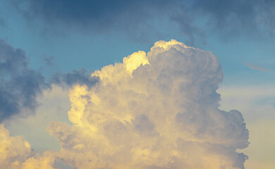 Golden-yellow clouds glow in the evening sky, illuminated by the warm rays of the setting sun,...