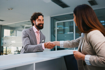 Businessman and businesswoman shaking hands at reception desk in modern office