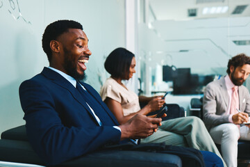 Excited businessman using smartphone in waiting room with colleagues