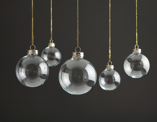 Clear glass Christmas ornaments hang from gold strings against a dark background, creating a minimalist and elegant holiday-themed composition with soft reflections and symmetry.

