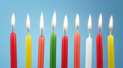 Vibrant row of nine lit candles in red, yellow, green, orange, and white against a calm light-blue background with flickering flames and charred wicks.