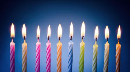Row of colorful lit birthday candles with varied striped patterns against a gradient blue-to-black background, emitting warm glowing flames and creating a festive celebratory ambiance.