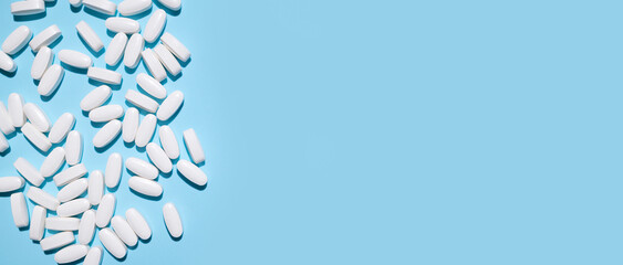 White oval tablets, vitamins, pills on blue background top view. Medical concept, minimalistic...