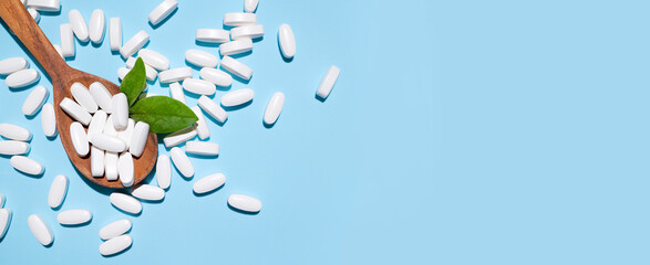 White tablets, vitamins, pills and green leaf in wooden spoon on blue background top view. Medical...