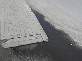Puddles form at the edge of a sidewalk on a cloudy day in an urban area after a recent rain shower