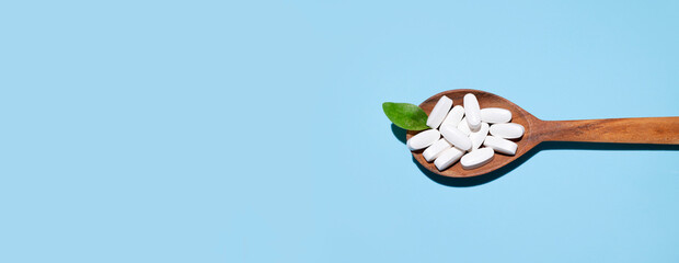 White tablets, vitamins, pills and green leaf in wooden spoon on blue background top view. Medical pharmaceutical background, health concept, organic dietary supplements, self care