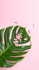 Pink pills scattered on a large green leaf against a pastel pink background, aesthetic pink flatlay