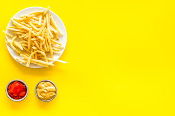 Fast food symbol. French fries on plate on yellow table top-down copy space