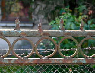 Old rusty fence with circular patterns and sharp spires in a garden setting