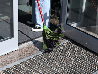 Cleaning entrance of building with mop and attention to detail during bright daylight hours