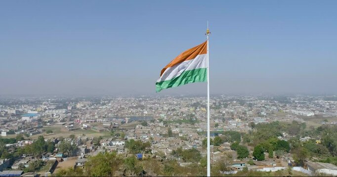 A beautiful cinematic shot of a weaving indian flag at the top of a semi-urban city.
