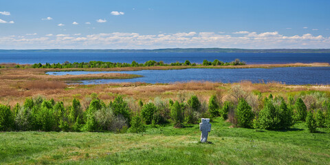 Stone cross on a hill overlooking a lake and wetlands.