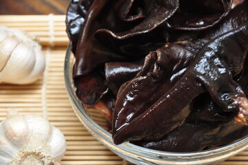 A close-up of a clear glass bowl filled with dark, translucent wood ear mushrooms. 