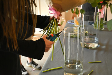 Hands carefully trim flower stems with scissors while assembling a bouquet.