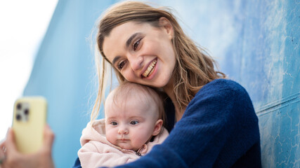 Mother and baby taking a selfie, both framed against blue wall