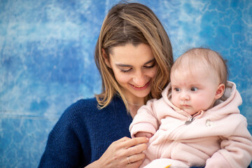 mother looks down warmly at her baby, who is in a soft pink outfit against blue wall