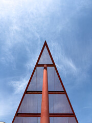 Abstract view of a red triangular metal structure with grid pattern, photographed from below against a bright blue sky, ideal for architecture and design inspiration.