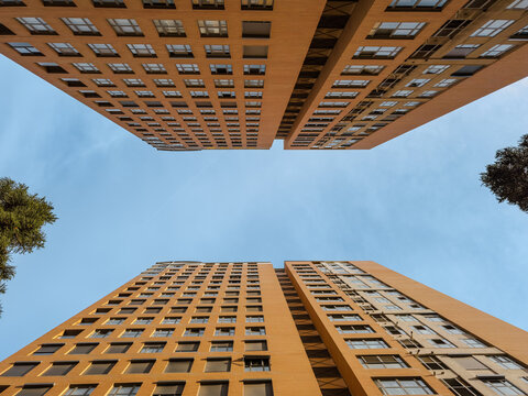 Dramatic upward perspective of tall modern apartment buildings with orange facades, clear blue sky, and geometric symmetry, ideal for urban architecture and city living concepts.