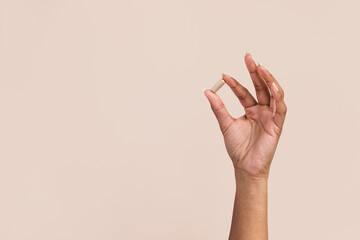 Black woman holding supplement pill in hand on tan background with copy space