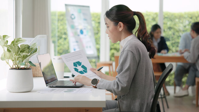 The way forward save the planet earth Gen Z female asia people go green net zero waste control ESG audit office desk. Young adult woman asian SDG carbon credit tax auditor busy happy work using laptop